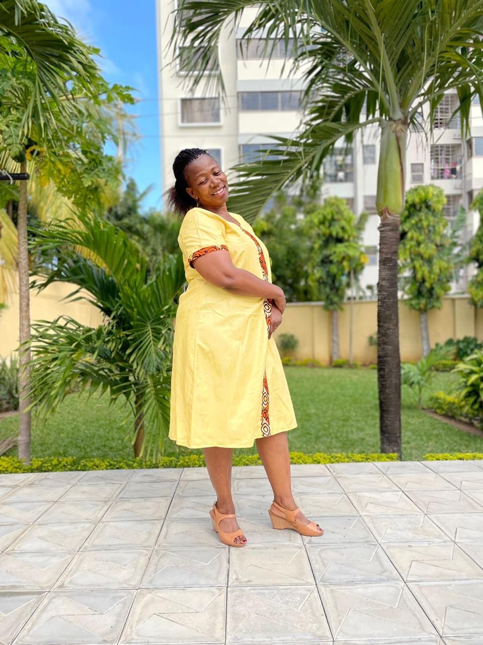 Caroline Mami Walter wearing a yellow dress with kitenge trim in a garden